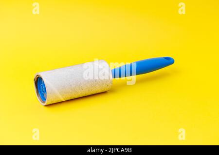 A blue lint roller with dust on it isolated on the yellow background Stock Photo