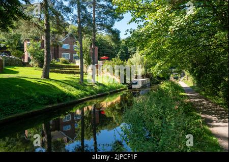 Narrowboat moored on the Caldon canal in Staffordshire in bright sunshine amongst trees and shrubs. Stock Photo