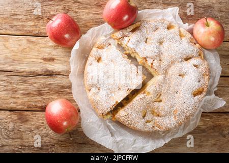 Sliced Apple pie sharlotka and red apples on a wooden table. Horizontal top view from above Stock Photo