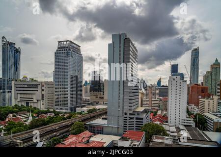 Bangkok, Thailand - 12 August 2022 - Aerial view of Bangkok cityscape showing high-rises and running BTS skytrains with cloudy blue sky Stock Photo