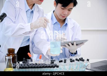 A smart and professional Asian male scientist or medical technician works with his senior female supervisor in the lab and records an experiment resul Stock Photo