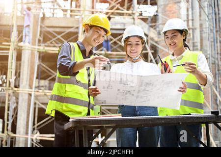 A team of professional young asian engineer working together at the construction site, checking the blueprint and discussing the construction plan. Stock Photo