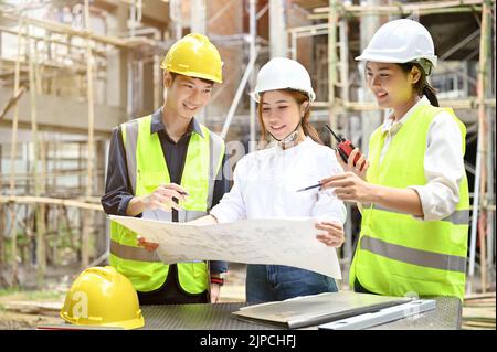 A team of professional young asian engineer checking the blueprint and working with a businesswoman at the construction site. Stock Photo