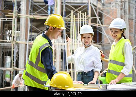 A beautiful Asian businesswoman having a outdoor meeting with two professional asian engineers in the building construction site. Stock Photo