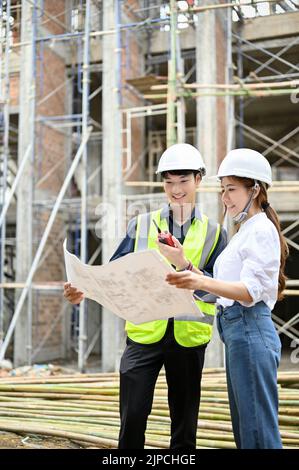 Portrait, Professional young asian male engineer and female architect in the construction site, looking and checking the building blueprint together. Stock Photo