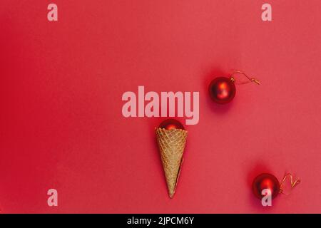 Christmas decoration in a waffle cone on a red background. Round toys with gold thread. Alternative Concept of celebrating winter holidays, top view festive composition. Flat lay Stock Photo