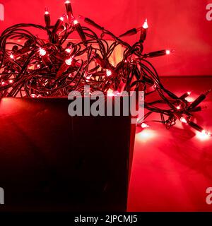 Fairy lights  lit  in cardboard box . Red background. Stock Image. Stock Photo