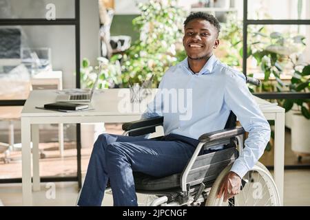 Portrait of African businessman with disability sitting in wheelchair and smiling at camera during his work at office Stock Photo