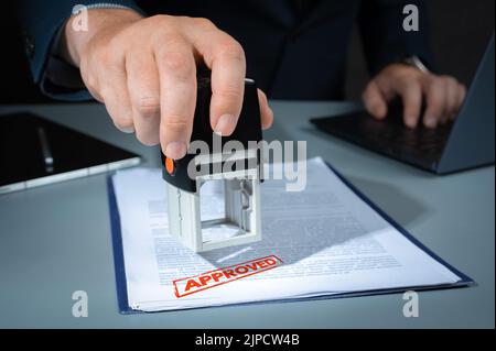 approved stamp . Close-up Of Person Hand Stamping With Approved Stamp On Document At Desk. businessman appoval stamper stamp on paper business contrac Stock Photo