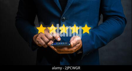 Businessman pointing five star symbol to increase rating of company. Man Evaluating Mobile Application On Smartphone With Five Stars. Customer review Stock Photo