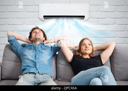 Happy couple sitting on sofa under air conditioner at home Stock Photo