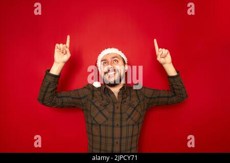 portrait of smiling man in Christmas hat casual clothes pointing his index fingers up at empty space Stock Photo