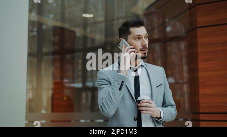 Stedicam shot of cheerful businessman talking with smartphone and walking in modern office hall indoors Stock Photo