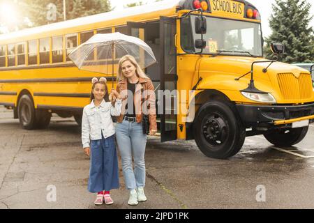 Back to school. Pupils of primary school near school bus. Happy children ready to study. little girl with mom going to bus Stock Photo