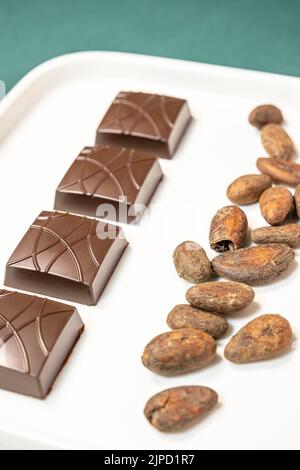 Handmade bitter chocolates on white plate with cocoa beans on green background. Stock Photo