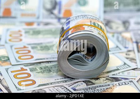 Bundle of money roll of dollars on a pile of 100 $ banknotes, stack of one hundred dollars American cash money bills rolled up with rubber band with a Stock Photo