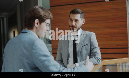 Two businessman colleagues standing and chatting standing near railing in hall of modern business center indoors Stock Photo