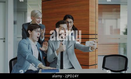 Happy business team taking selfie portrait on smartphone camera and posing for group photo during meeting in modern office indoors Stock Photo