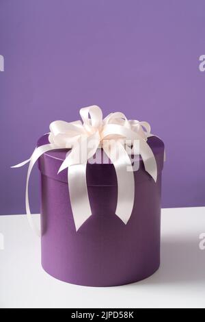 A purple round box with a white puffy bow on a white table. Holiday concept. Stock Photo