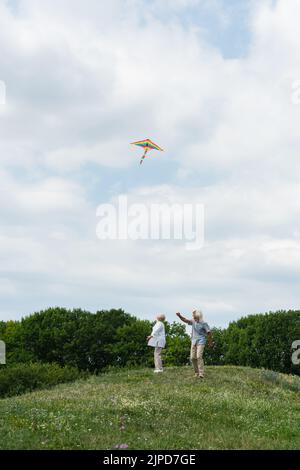 happy senior couple in casual clothes looking at flying kite in cloudy sky Stock Photo