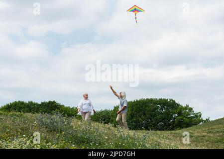 happy senior couple in casual clothes playing with kite on green hill Stock Photo