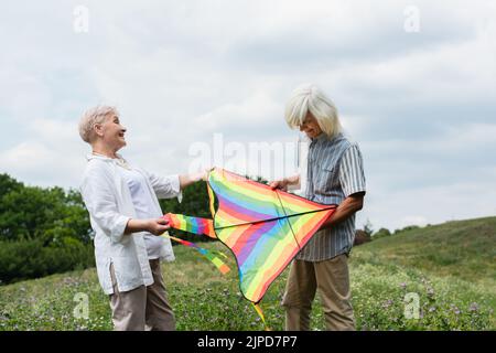 happy senior couple in casual clothes holding kite on green hill Stock Photo