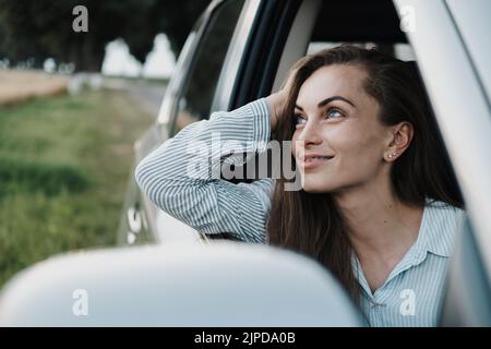 Cheeful caucasian woman with braces enjoying road trip and looking out from car window Stock Photo