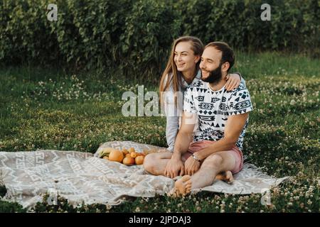 Cheerful man and caucasian woman sitting on blanket and enjoying weekend picnic together, happy middle-aged couple having picnic outside the city Stock Photo