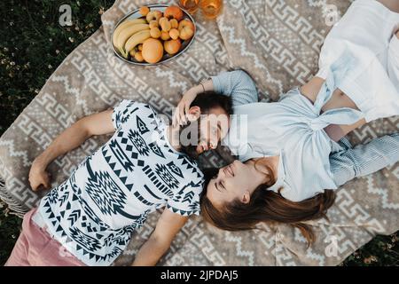 Top-down shot of cheerful man and caucasian woman laying on blanket and enjoying weekend picnic together, happy middle-aged couple having picnic Stock Photo