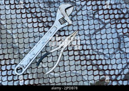 Adjustable wrench and pliers on a metal rusty grid Stock Photo