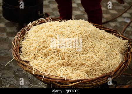 Chinese Schezwan Also Called Szechwan Veg Hakka Noodles Chowmin or Indian Veg Chow Mein Being Washed Rinsed In Water In Bamboo Basket. Dhaba Style Stock Photo