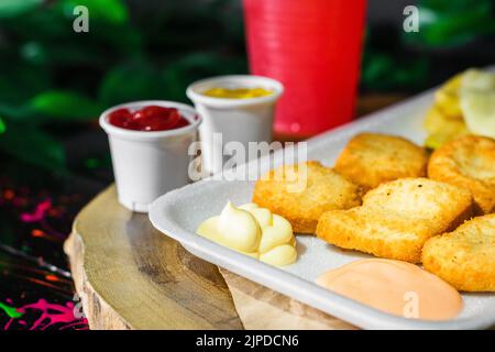 close-up detail of a plate of chicken nuggets with potatoes and mozzarella cheese, served on a wooden tray with a glass of red fruit juice next to it, Stock Photo