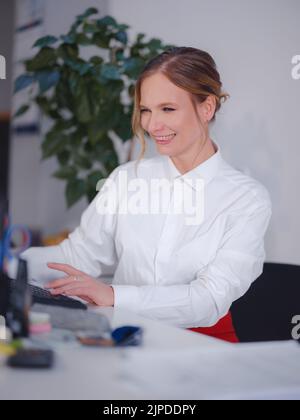 Successful female graphic designer watching textbook about creative ideas on laptop while working process in office. Positive student with blond hair is reading business news on netbook Stock Photo