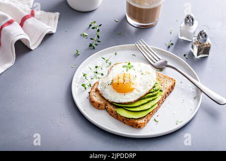 Avocado toast on a toasted multigrain bread with a fried egg Stock Photo