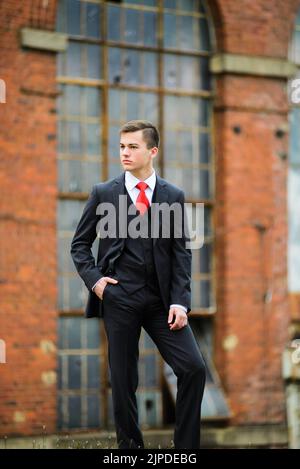 Handsome young dark haired male in a dark business suit and tie in front of old architecture . Stock Photo