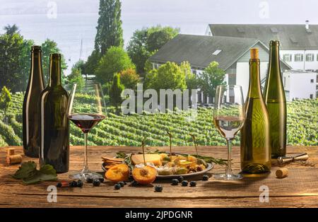Bottles and glasses of red and white wine with delicious appetizers, olives, cheese and honey, fruits and berries lying on table. Countryside vineyard Stock Photo