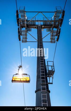 Empty ski-lift chair and cable car mast on blue sky background Stock Photo