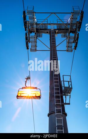 Empty ski-lift chair and cable car mast on blue sky background Stock Photo