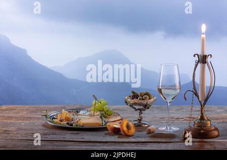 Vintage image of wine bottle, glass filled with delicious white wine isolated over beautiful nature landscape of mountains. Winemaking on countryside Stock Photo