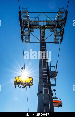 Skiers sitting at ski-lift chair and cable car mast on blue sky background Stock Photo