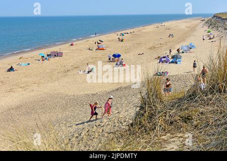 Winterton-on-Sea people on sandy sunbathing beach beyond dunes  coarse grass planted to help reduce erosion from North Sea storms Norfolk England UK Stock Photo