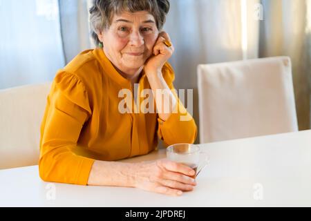 Old retired gray-haired woman in yellow blouse. Stock Photo