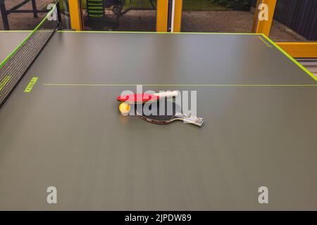 Close up view of two ping-pong rackets and orange plastic ball on green tennis table on villa's front yard. Active lifestyle concept. Sweden. Uppsala. Stock Photo