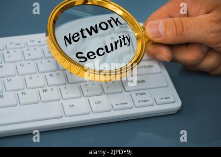 White computer keyboard, magnifier in hand and the inscription network security, Concept of the risk associated with inattentive use of the Internet Stock Photo