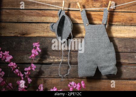 baby clothes hanging from a clothesline rope tied with wooden hooks, overalls and hat with ears knitted in the technique of hand crochet, on a backgro Stock Photo