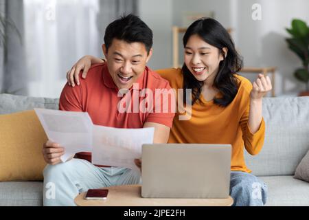Emotional asian spouses reading papers, using laptop Stock Photo