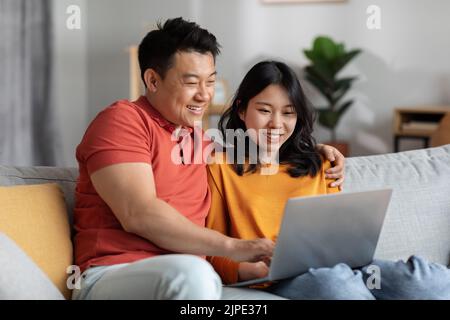 Asian spouses watching movie on Internet, using laptop Stock Photo