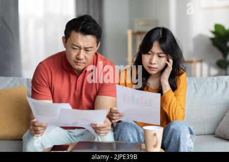 Confused asian couple checking bills, home interior Stock Photo