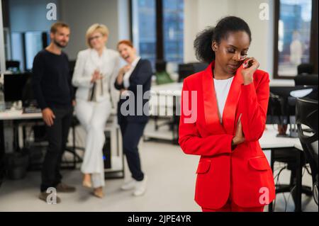 Young african woman crying because of the ridicule of colleagues. Racial discrimination in the office. Stock Photo