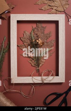 bouquet from dried pressed leaf in frame with scissors, rope and notebook on brown background. hobby, handmade , floral art and boho style concept. Stock Photo